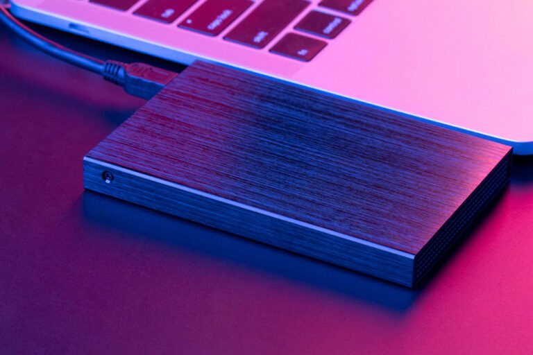 HD externo preto conectado a um Macbook Pro em uma mesa escura iluminada com uma luz violeta.