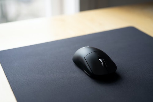Mouse Logitech preto em cima de um mousepad preto em uma mesa de madeira.