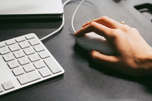 Homem segurando um mouse branco em uma mesa preta ao lado de um teclado Apple.