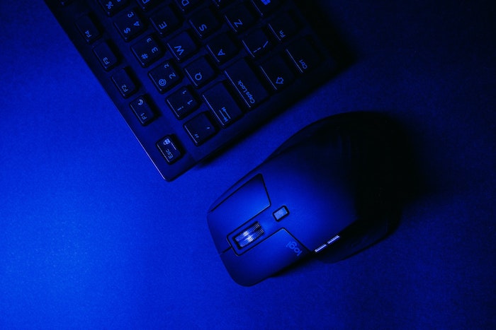 Mouse Logitech preto em uma mesa escura, ao lado de um teclado preto sob iluminação azul.