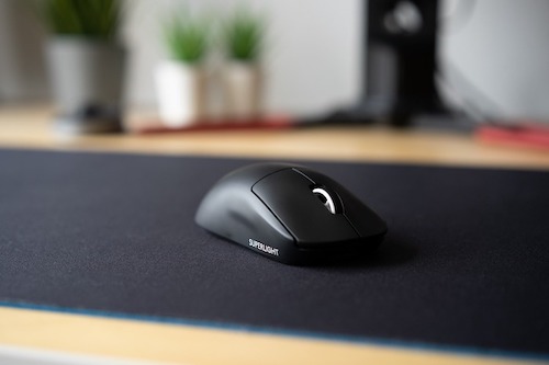 Mouse Logitech preto em cima de um mousepad preto em uma mesa de madeira.
