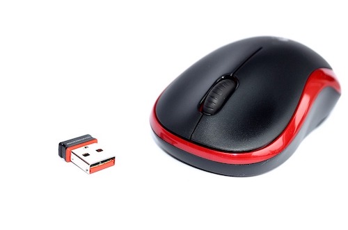 Mouse Logitech preto e vermelho em uma mesa branca ao lado de seu adaptador USB bluetooth.