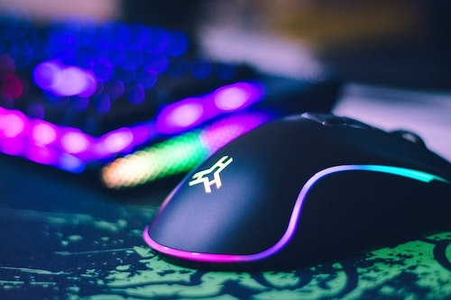 Mouse preto gamer com leds coloridas ao lado de teclado iluminado a base de leds.