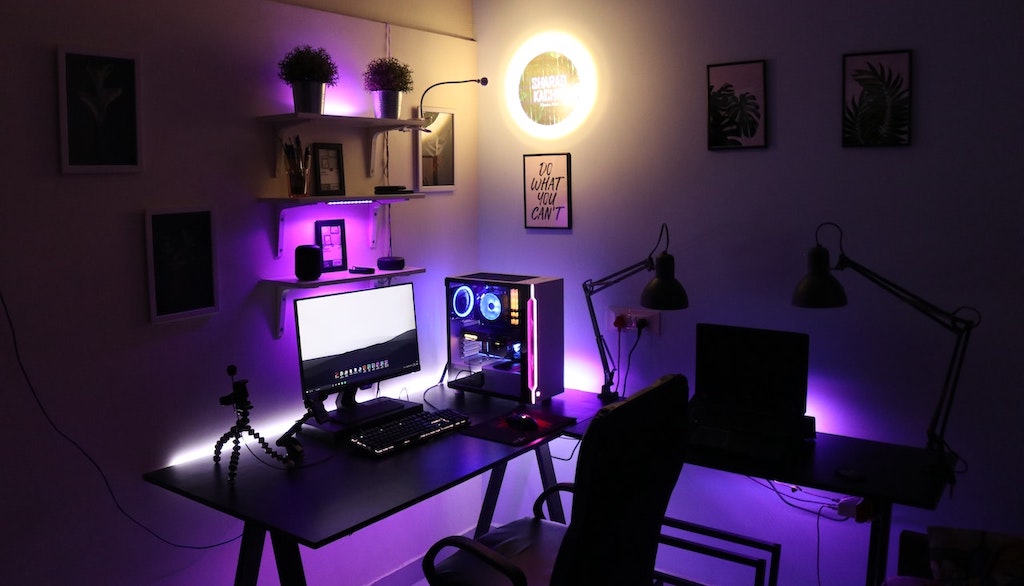 Setup gamer com bastante leds roxos em quarto com pouca iluminação. Computador com gabinete transparente mostrando placas de vídeo.