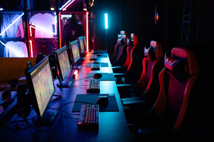 Computadores Gamers enfileirados, com teclados gamers e mouses gamer com leds coloridas em ambiente escuro.