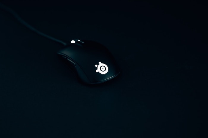 Mouse gamer preto com led branco em ambiente escuro.