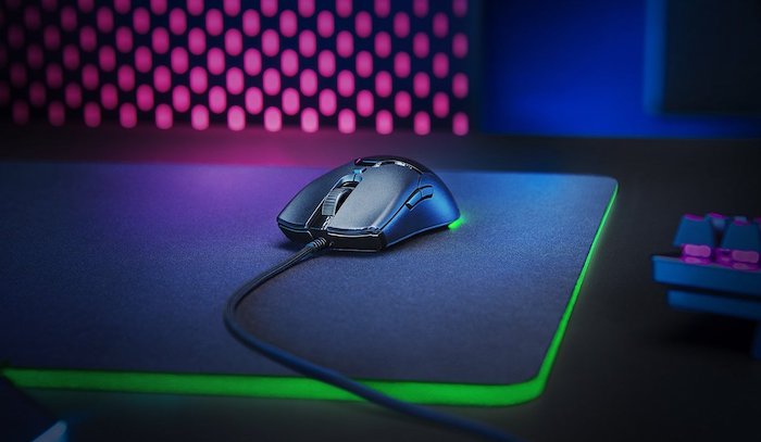 Mouse Razer preto com fio visto de frente em cima de um mousepad com leds verdes.