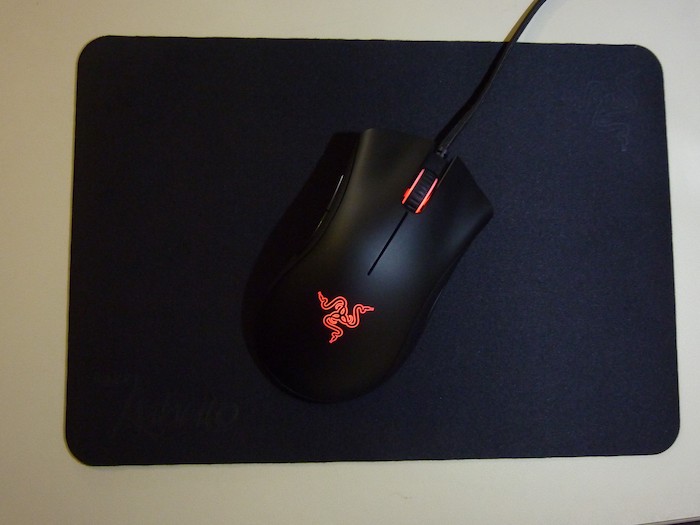 Mouse Razer preto com leds vermelhas visto de cima em mousepad preto.