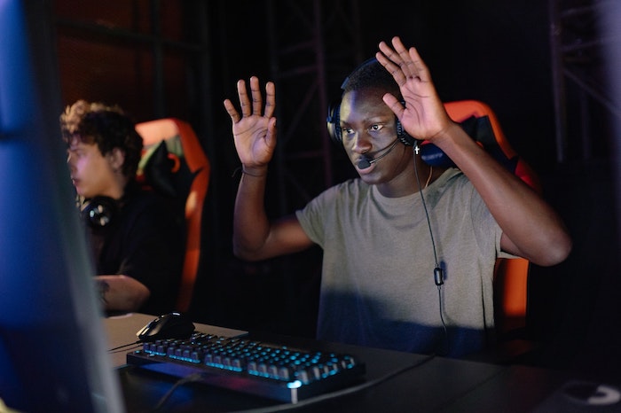 Homem de pele escura com mãos para cima jogando video game.