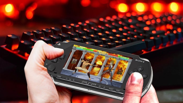 Homem jogando PSP. Um teclado mecânico preto com leds laranjas sendo mostrado ao fundo.
